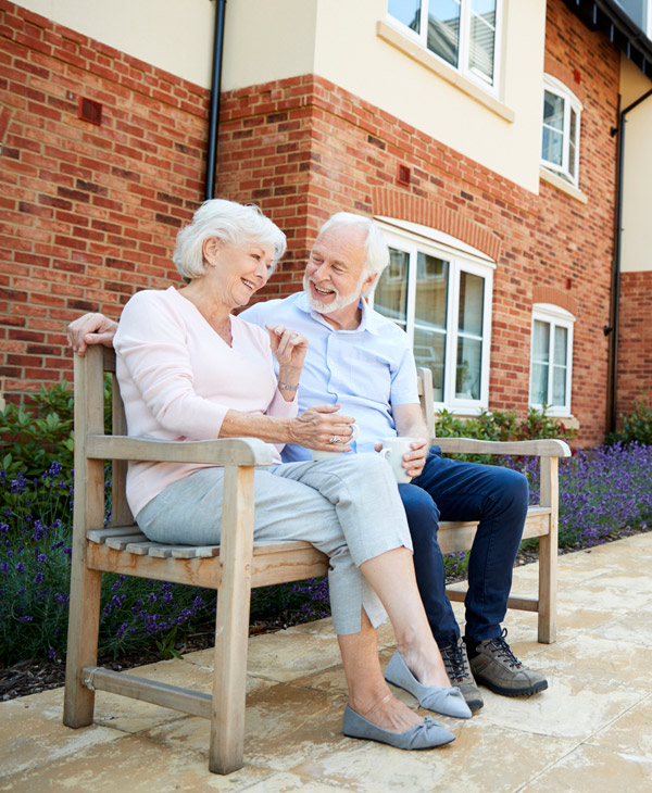 happy elderly couple sitting on bench at assisted living home