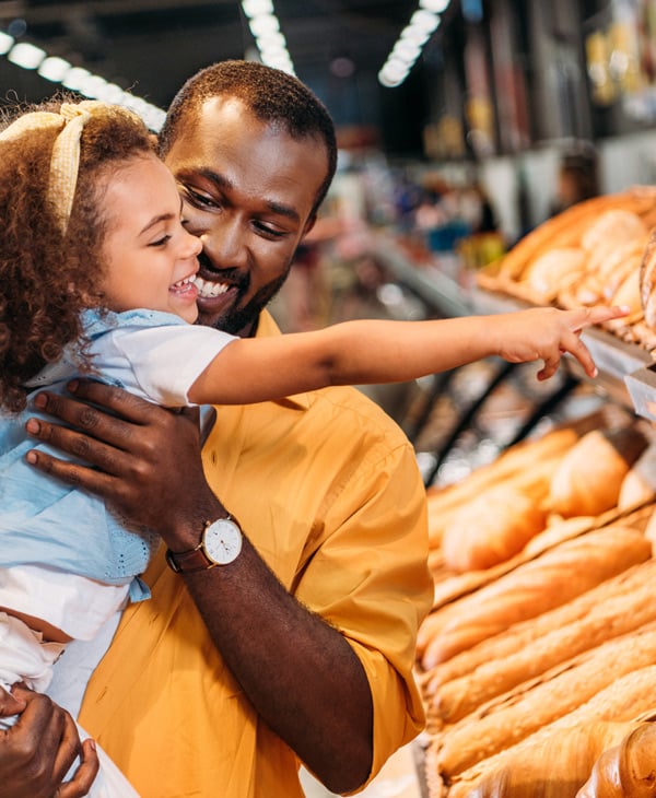 Man lifting daughter in store to select bread