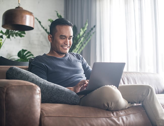 man sitting on couch smiling at laptop